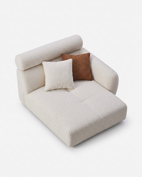 A modern low-profile daybed or chaise lounge upholstered in a textured cream bouclé fabric, styled with two throw pillows (one cream bouclé and one brown linen) on a clean white background.