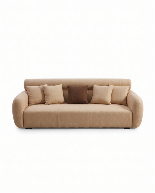A modern beige fabric sofa with rounded arms and backrest, styled with five throw pillows including four beige cushions and one dark brown accent pillow, shown against a plain white background.