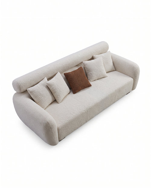 A modern low-profile sofa upholstered in a textured cream bouclé fabric, featuring a curved backrest, rounded arms, and four throw pillows including one contrasting brown square pillow, shown on a solid white background.