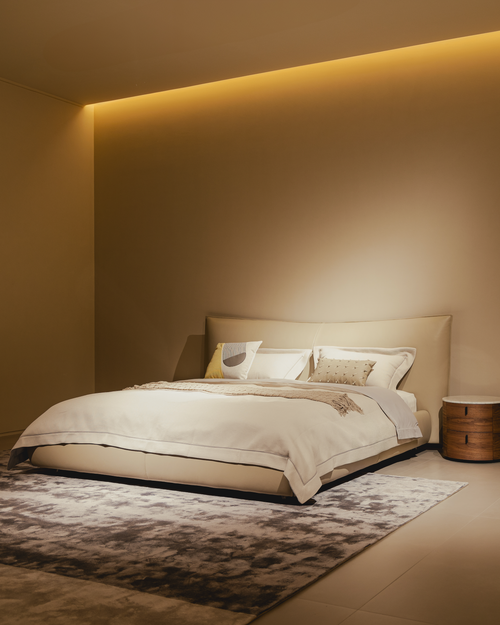 Modern bedroom with a bed and side table against a beige wall with ambient lighting.