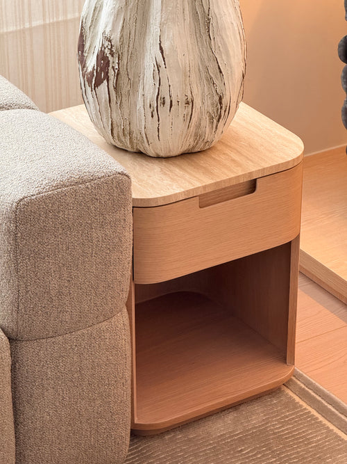 Wooden side table with a textured vase next to a gray sofa.