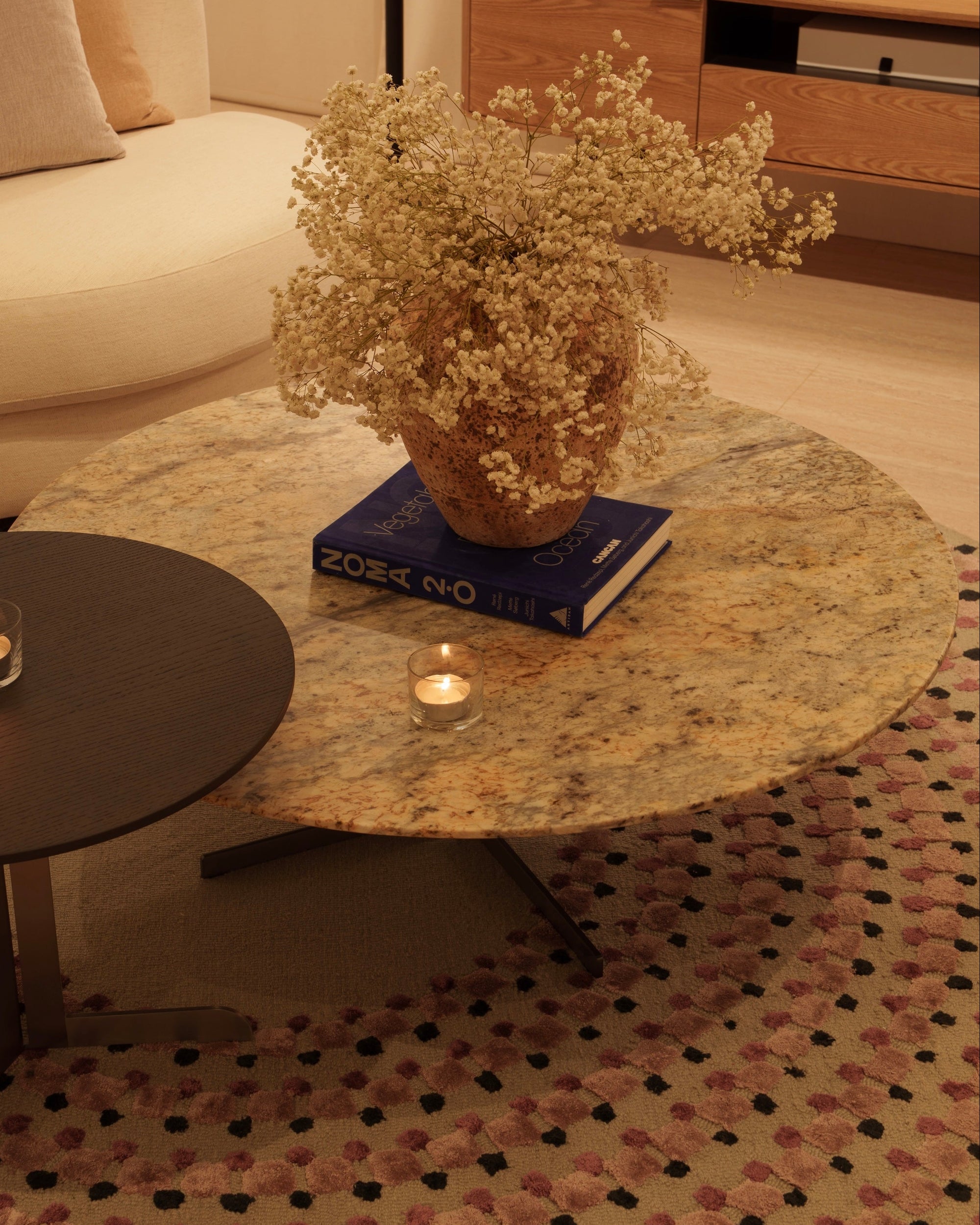 Round marble coffee table with a vase of flowers and books in a living room setting.