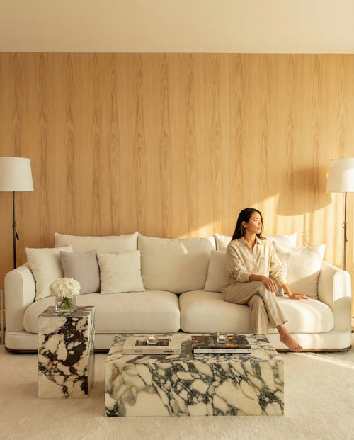 Woman sitting on a white sofa in a modern living room with marble coffee table and wooden wall.